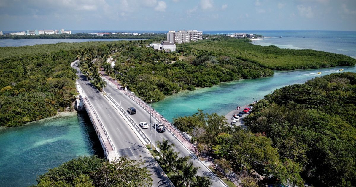 Vista aérea de un puente vehicular sobre un canal en Cancún, con manglar y hoteles de la Zona Hotelera al fondo